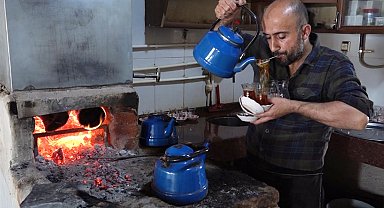 Çay taleplerine yetişmek için ağzında süzgeçle bardakları dolduruyor